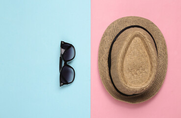 Straw hat and sunglasses on pink blue background. Top view