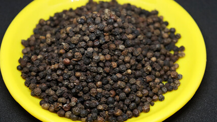 The pile of black pepper is on a black background on a yellow plate