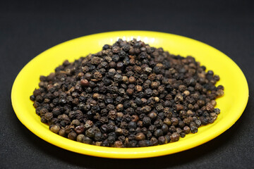 The pile of black pepper is on a black background on a yellow plate