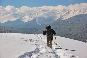 Hiker with backpack walking on snowy mountain hillside on cold winter day.