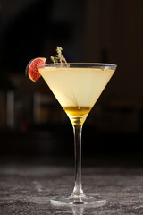 One martini glass with yellow alcoholic beverage liquor with thyme branch, honey and figs on grey table, dark bar background