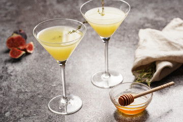 Two martini glasses with yellow non-alcoholic beverage lemonade with thyme branch, honey and figs...