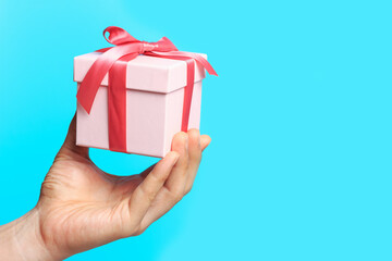 Male hand holding a gift box isolated on blue background, copy space.