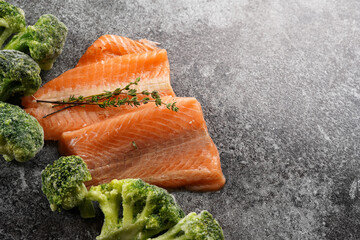 Two red raw salmon steaks and broccoli on a grey marble surface, top view, negative space