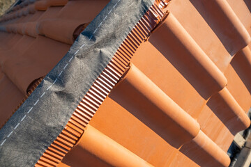 Closeup of yellow ceramic roofing ridge tiles on top of residential building roof under...