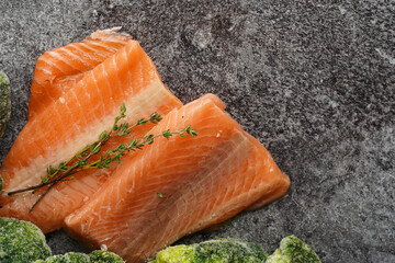 Two red raw salmon steaks and broccoli on a grey marble surface, top view, negative space