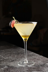 One martini glass with yellow alcoholic beverage liquor with thyme branch, honey and figs on grey table, dark bar background