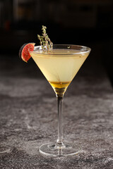One martini glass with yellow alcoholic beverage liquor with thyme branch, honey and figs on grey...