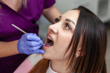 Young woman being examined by the stomatologist. Beauty female sitting in medical chair while dentist fixing her teeth at dental clinic. Dentist examining patient's teeth