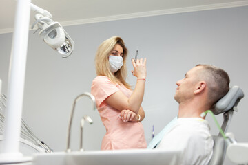 Woman dentist holds a syringe with anesthesia. Handsome Caucasian Man Sitting in Medical Chair at Dental Clinic