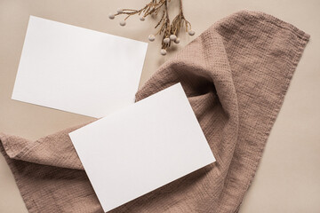 Blank clipping path paper sheet card with mockup copy space and dry floral branch and blanket cloth on neutral beige background. Minimal aesthetic business brand template. Flat lay, top view