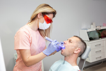 Professional dentist makes teeth whitening procedures to male patient in dental clinic