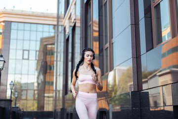 Beautiful fit woman runner with pigtails jogging against the background of a city building