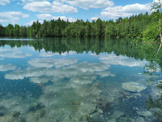 Fototapeta premium The shore of the lake is bright with clear water, in which you can see the marble on the bottom and reflect the sky with clouds, in the mountain park Ruskeala.