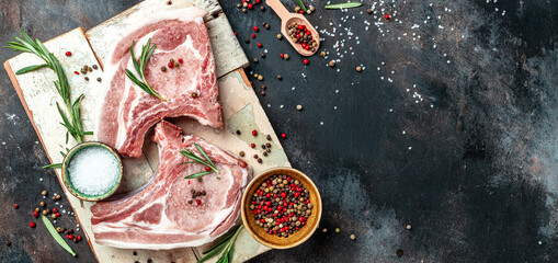 Organic Pork meat chop set with spices and rosemary and red pepper on black table. Long banner format. top view