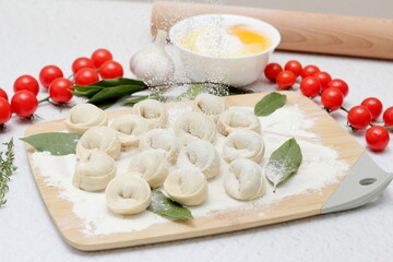 handmade dumplings on a wooden board are sprinkled with flour, next to tomatoes, bay leaf, garlic