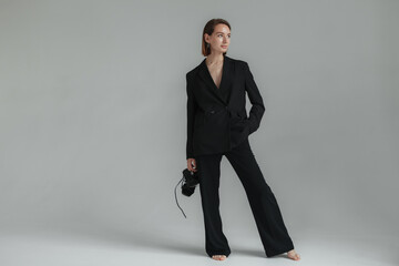 Stylish young woman in a suit on a naked body holds sandals in her hands in a gray studio