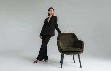 Fashion shot of young stylish woman in black suit with armchair in the studio. Vogue, Lifestyle