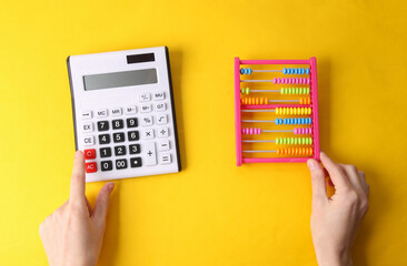 Hand holds children's colored abacus and calculator on yellow background