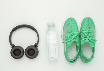 Sports shoes, water bottle and stereo headphones on a white background. Getting ready for training. Top view. Flat lay