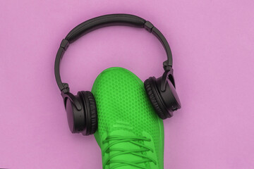 Green sports shoe with stereo headphones on pink background. Top view