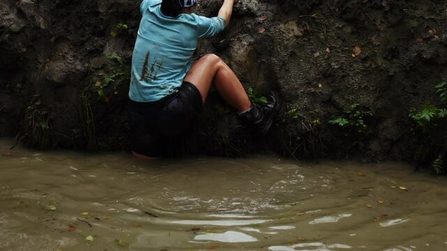 Overcome obstacle courses in water and mud. Participants make their way through a ditch during the race. Slow motion