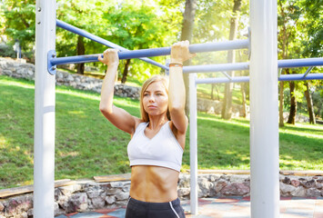 Fototapeta premium Fit slim woman pulls herself up on horizontal bar on an outdoor sports ground