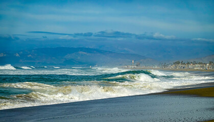 Beautiful coast with rough seas large waves and people in the background, mountains and clouds