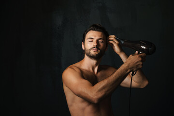 Young half-naked man posing on camera while using hair dryer