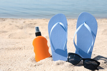 Stylish flip flops, sunglasses and sun protection spray on sandy beach