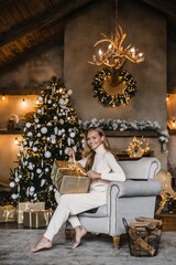 Obraz na płótnie Canvas young beautiful woman model with long hair in a beige suit christmas tree christmas In brown wooden houses 