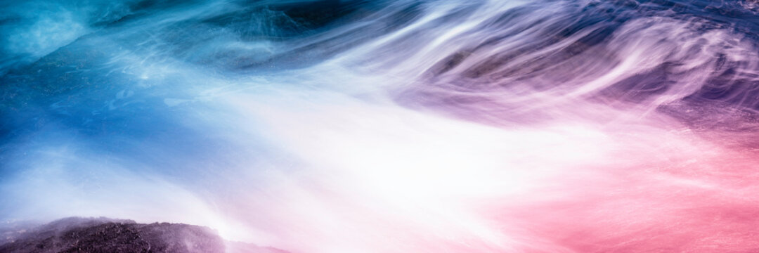 White waves flow over the red and blue seawater. Abstract panoramic seascape background image with space for text and design. Rocky beach landscape with motion blur effect of long exposure photography