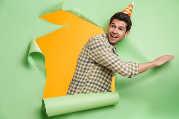 Young unshaven man smiling while posing into hole in green background