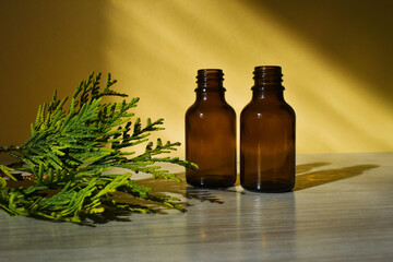 dropper bottle of brown glass and branch thujas against the yellow background. Beauty products packaging. Copy space. High quality photo