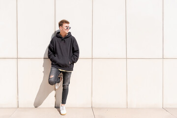 Young man in black sweatshirt posing with his sunglasses outdoors