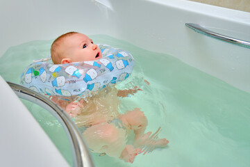 Infant swimming, a frightened boy swims in a home bath with an inflatable ring on his neck