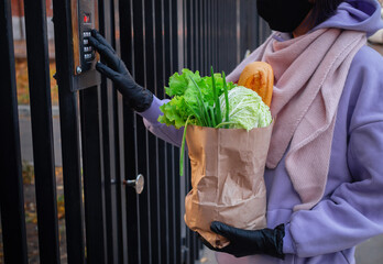 A girl in a black mask delivers a paper bag of products. Delivery person and door bell with...