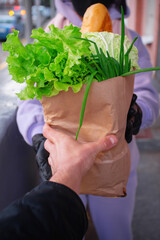 A girl in a black mask delivers a paper bag of groceries to a man customer. Ordering groceries from an online store. Home delivery food during virus outbreak, coronavirus panic and pandemics.