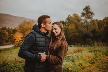 Man and woman hugging and kissing against autumn mountain forest