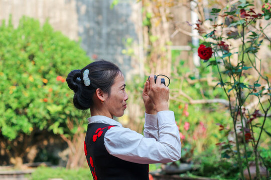 Vietnamese mid-age woman taking pictures with small camera in the garden