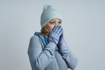 middle-aged woman in a gray hat, sweater, gloves hides her nose from the cold