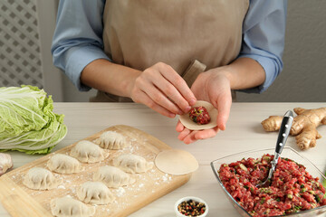 Woman making gyoza at white wooden table, closeup