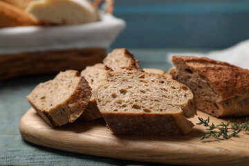 Fototapeta na wymiar Cut buckwheat baguette with thyme on light blue wooden table, closeup