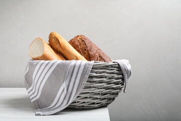 Different tasty baguettes in basket on white wooden table. Space for text