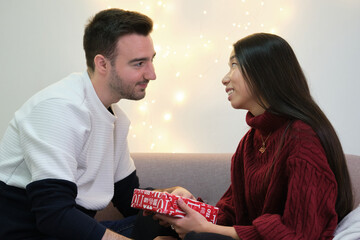 Young asian woman giving a Christmas present to his caucasian boyfriend.