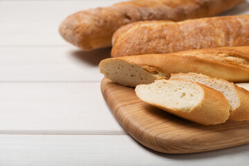 Cut tasty baguette on white wooden table. Space for text