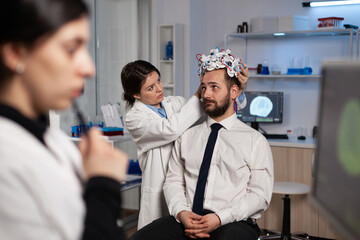 Specialist researcher woman putting eeg headset on man patient analyzing brain evolution monitoring nervous system activity in neurology laboratory. Doctor in neuroscience doing medical tomography