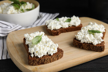 Obraz na płótnie Canvas Bread with cottage cheese and basil on black wooden table, closeup