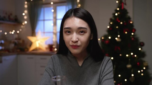 smiling attractive girl in knitted sweater near christmas tree in decorated home and calling friends with congratulations on xmas eve. cheerful woman face camera chatting on online video phone call