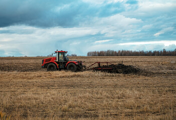 Red Russian Tractor Plows in the Dry Field. Corn Harvesting. Side View. Dramatic Clouds Sky. Cultivating Agriculture.